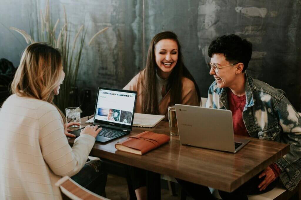 Group of three people laughing around a table with their laptops